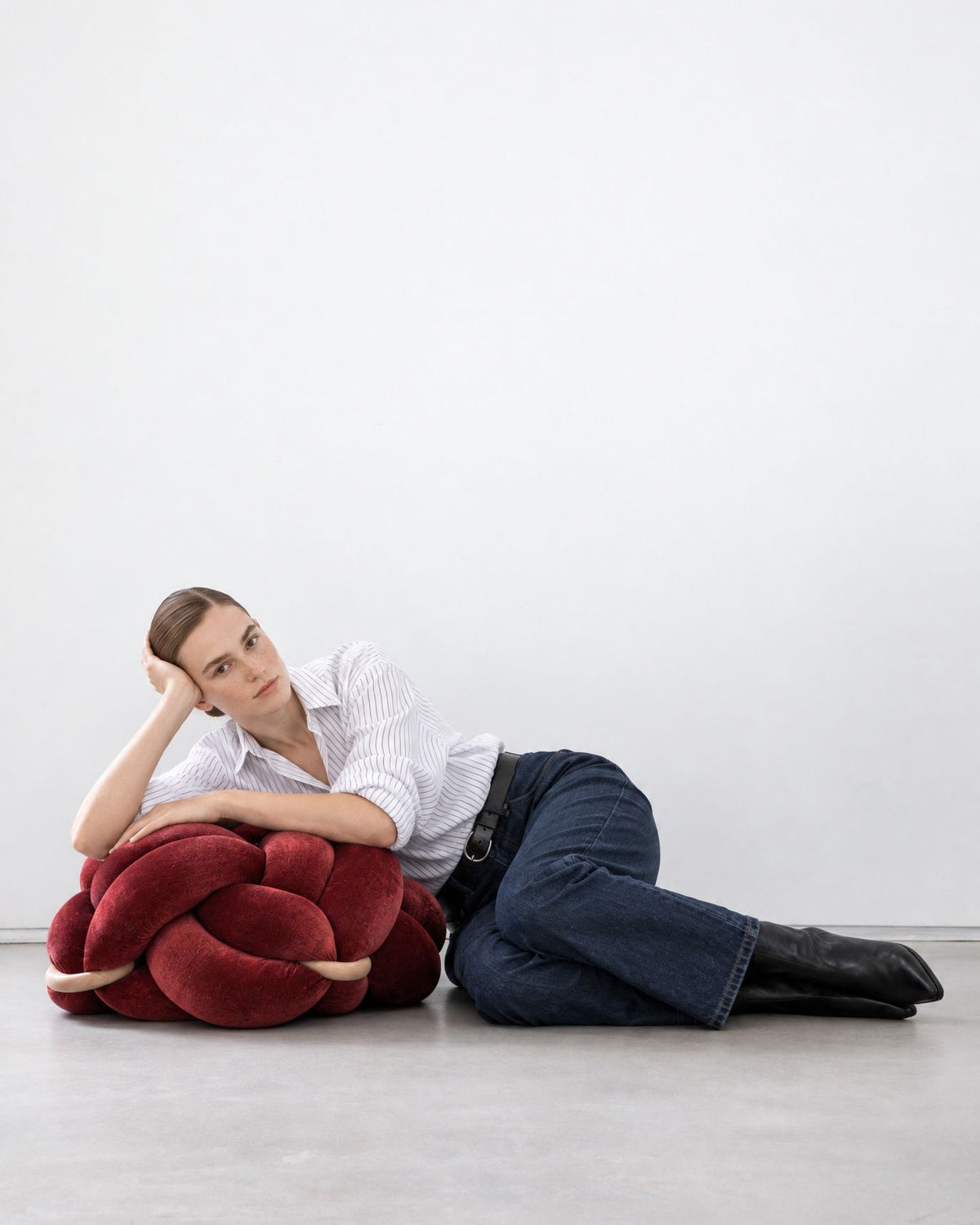 Woman lying on the floor leaning on a maroon velvet knot ottoman