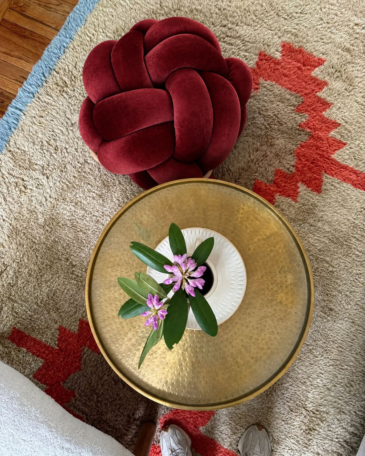 Top view of a maroon velvet knot ottoman beside a brass side table