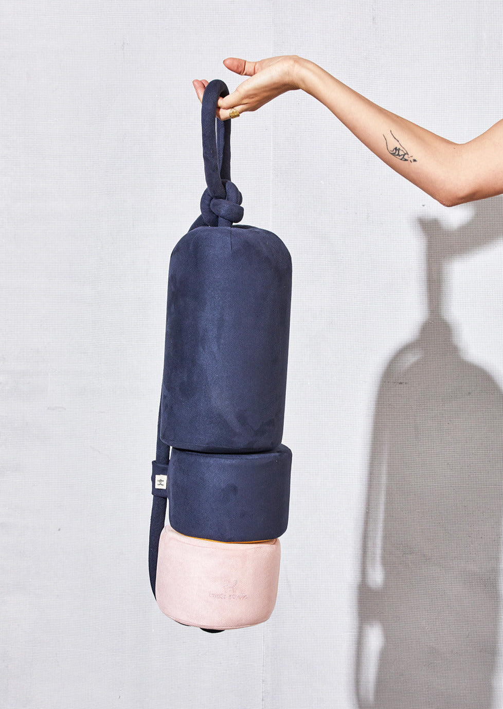 Hand holding a navy and pink Sailor's Buoy cushion by its strap