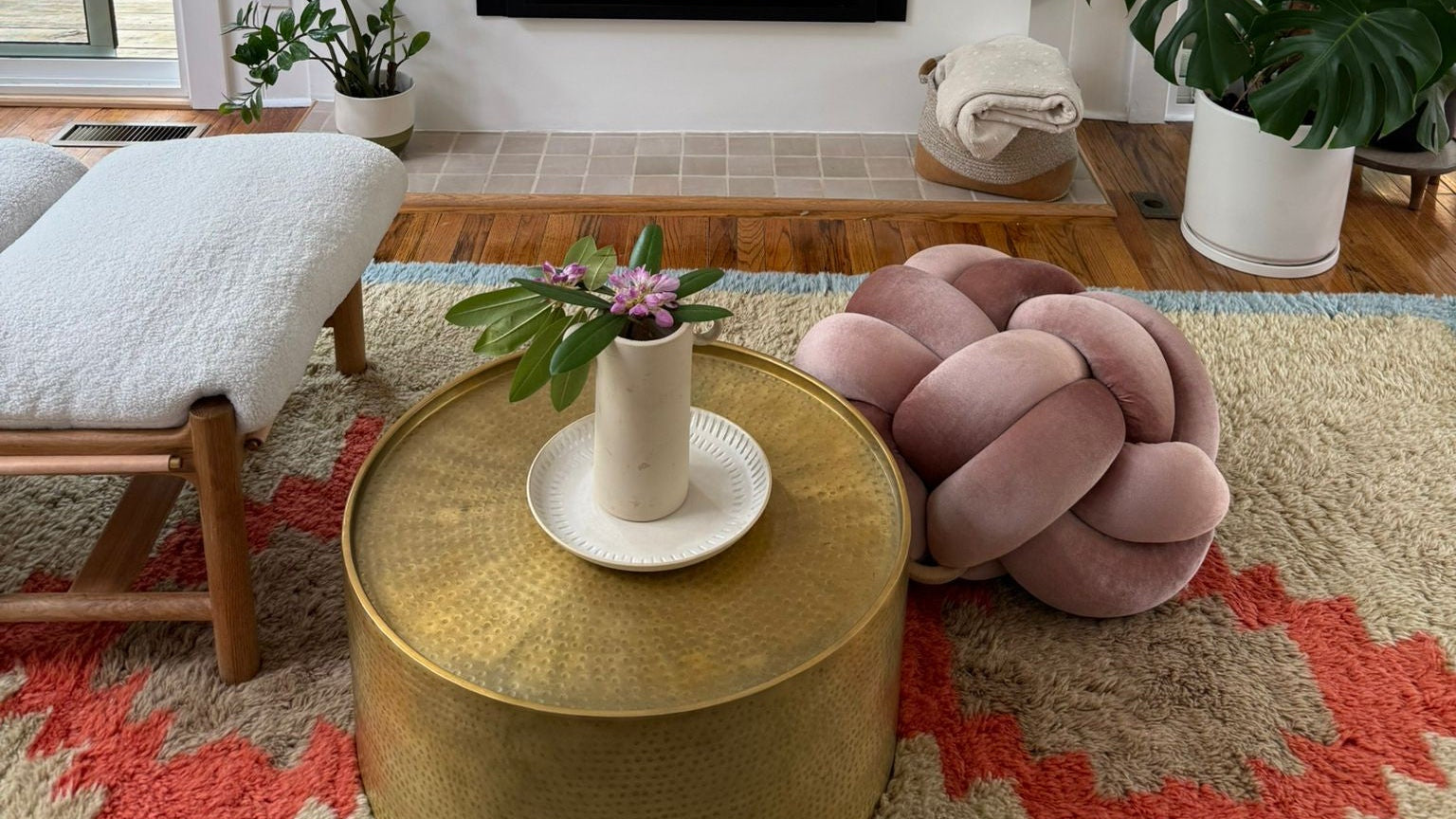 Living room with a fireplace, gold coffee table, pink pouf, and plants.