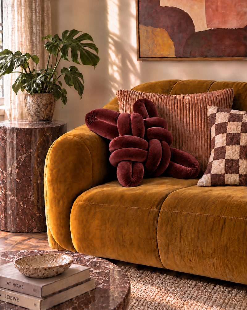 Maroon velvet knot pillow on a mustard velvet sofa