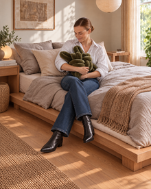 Woman sitting on a bed hugging an olive green velvet knot pillow
