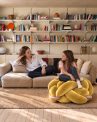 Mother and daughter relaxing with a large sunlight yellow velvet knot ottoman in a living room