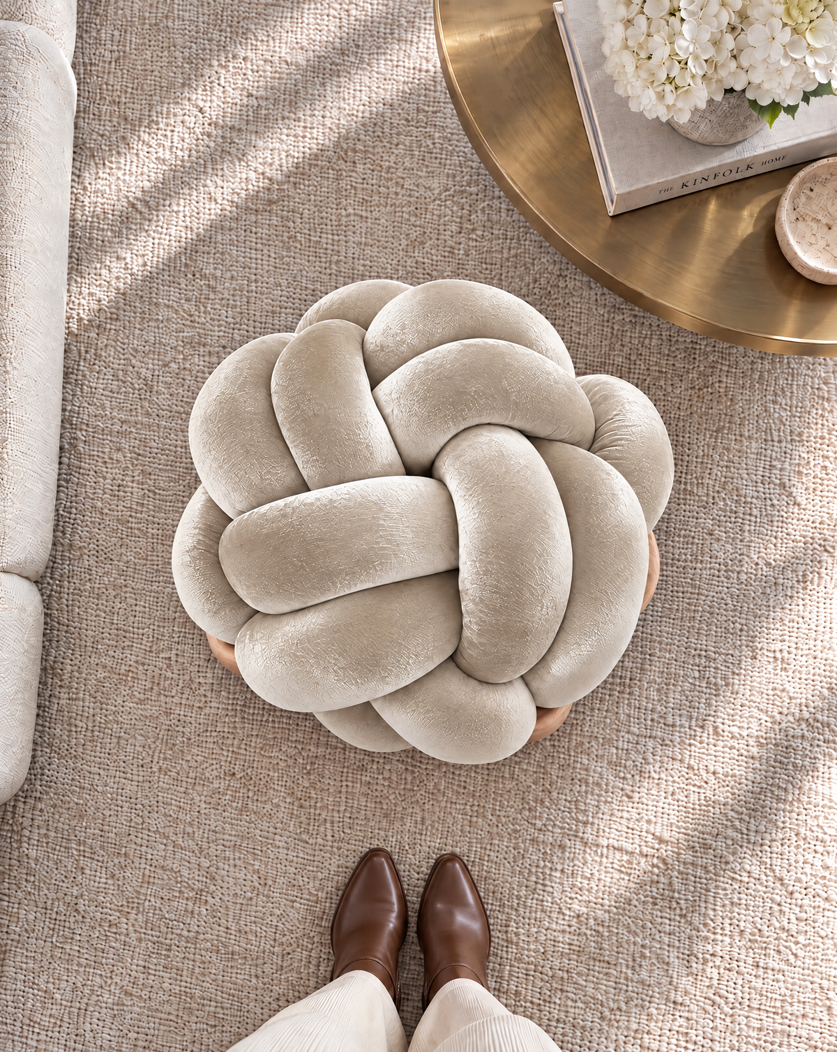 Top view of a pearl velvet knot ottoman beside a brass side table