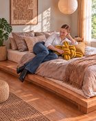 Woman relaxing on a bed with a sunlight yellow velvet knot pillow