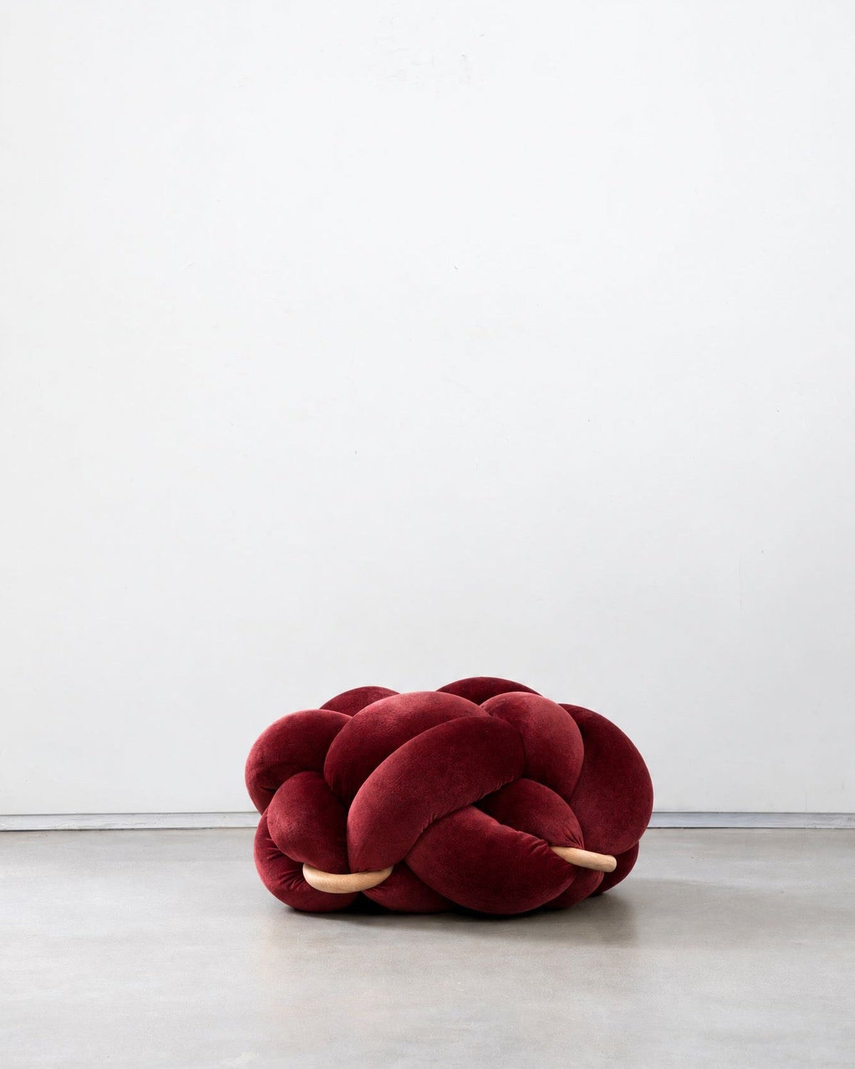 Maroon velvet knot ottoman on a concrete floor