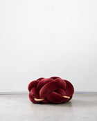 Maroon velvet knot ottoman on a concrete floor
