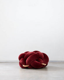 Maroon velvet knot ottoman on a concrete floor