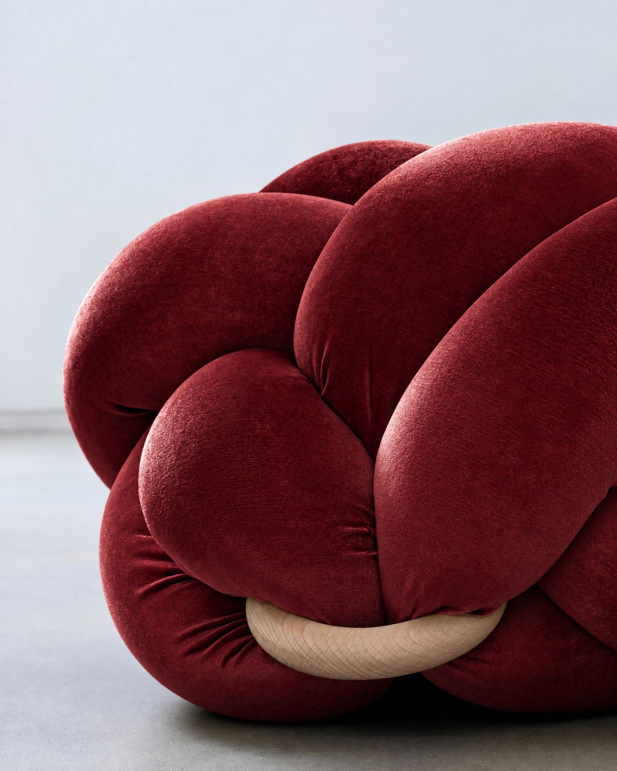 Close-up of a maroon velvet knot ottoman with its wooden ring
