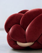 Close-up of a maroon velvet knot ottoman with its wooden ring