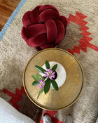 Top view of a maroon velvet knot ottoman beside a brass side table