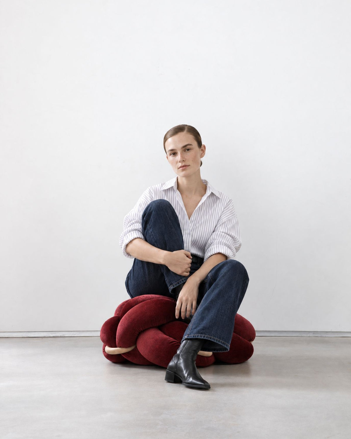 Woman sitting on a maroon velvet knot ottoman