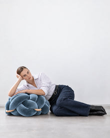 Woman lying on the floor leaning on an ocean blue velvet knot ottoman