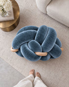 Top view of an ocean blue velvet knot ottoman beside a brass side table