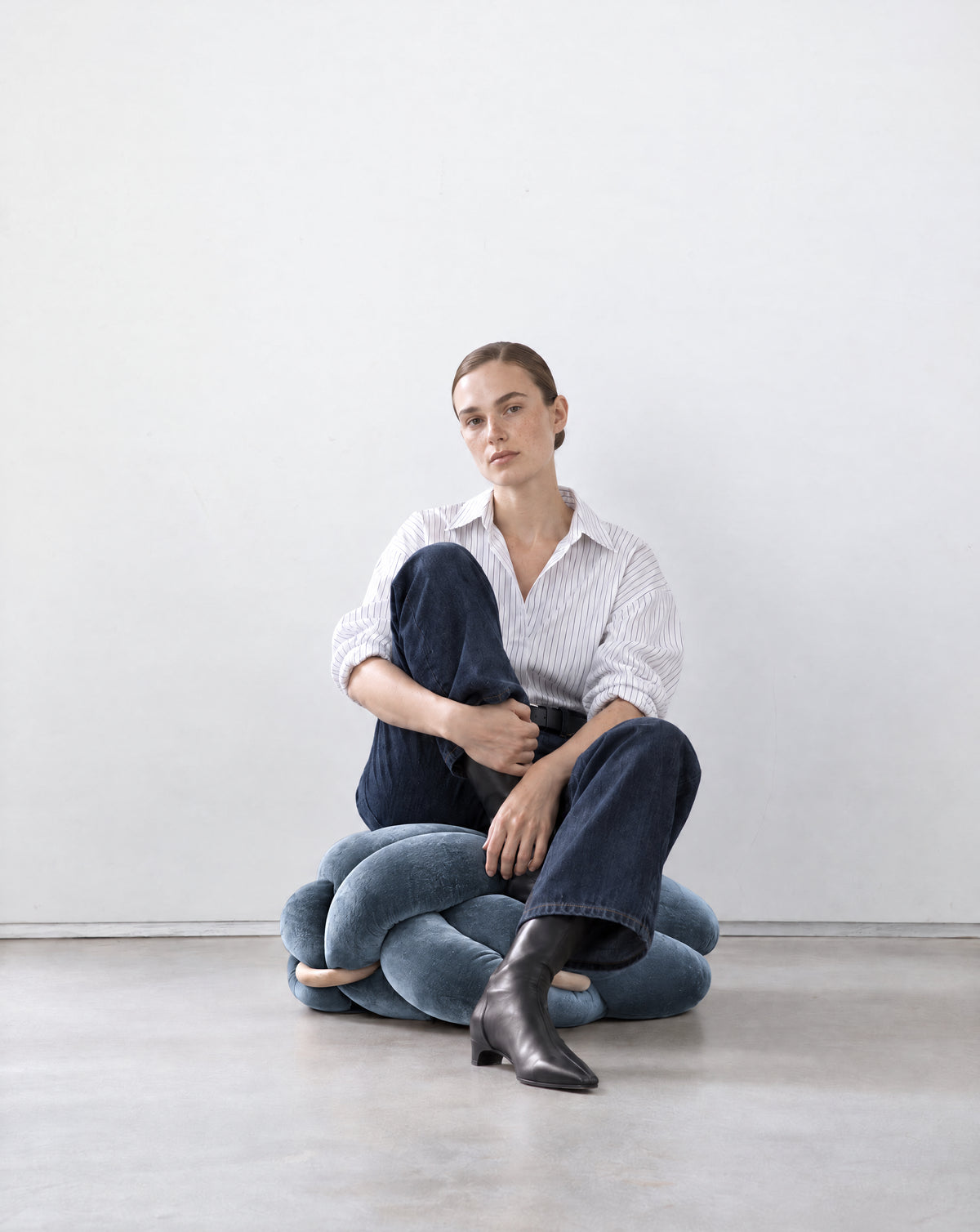 Woman sitting on an ocean blue velvet knot ottoman