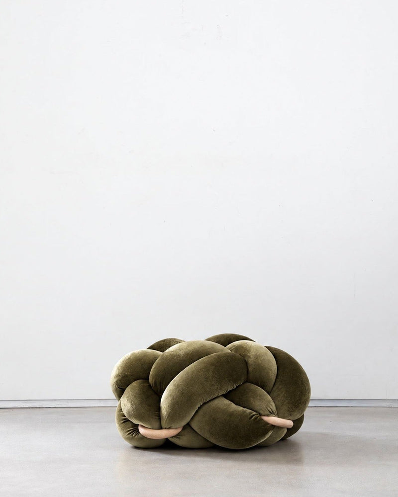Olive green velvet knot ottoman on a concrete floor
