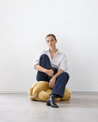 Woman sitting on a sunlight yellow velvet knot ottoman