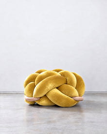 Large sunlight yellow velvet knot ottoman on a concrete floor