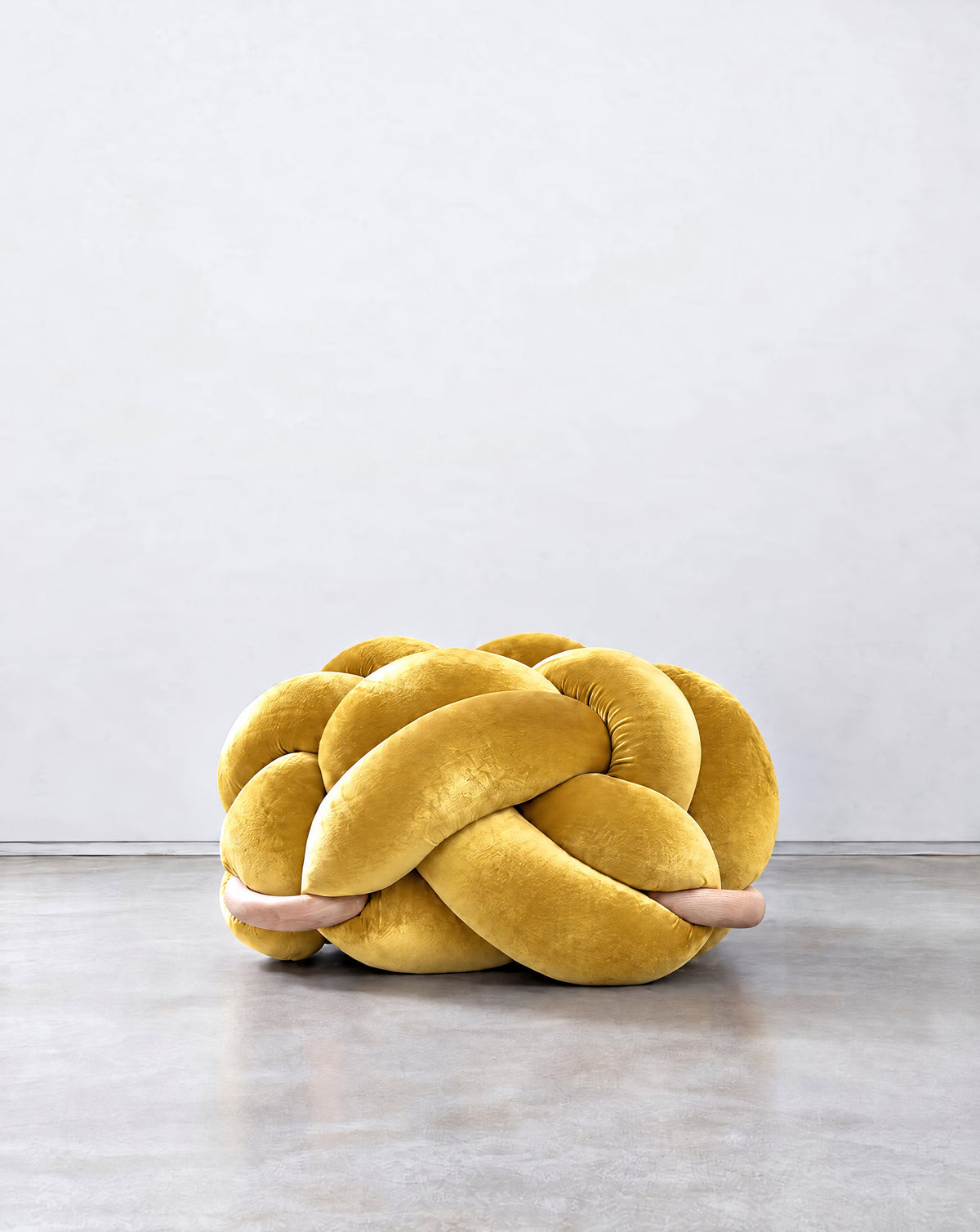 Large sunlight yellow velvet knot ottoman on a concrete floor
