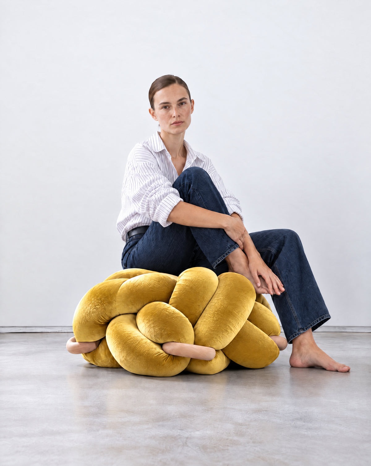 Woman sitting on a large sunlight yellow velvet knot ottoman