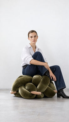 Woman sitting on a large olive green velvet knot ottoman
