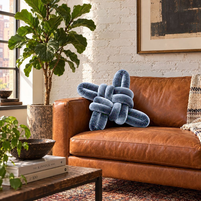 Navy blue velvet knot pillow on a leather sofa